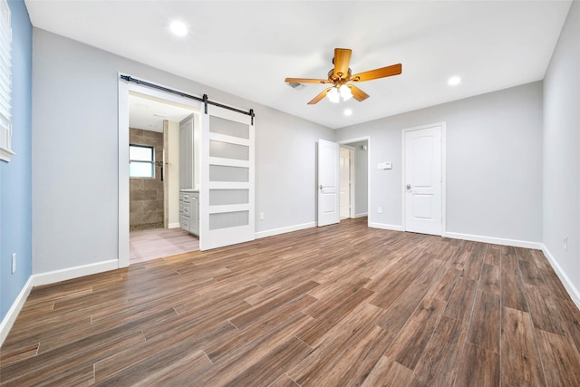 unfurnished bedroom featuring dark hardwood / wood-style floors, ceiling fan, ensuite bathroom, and a barn door