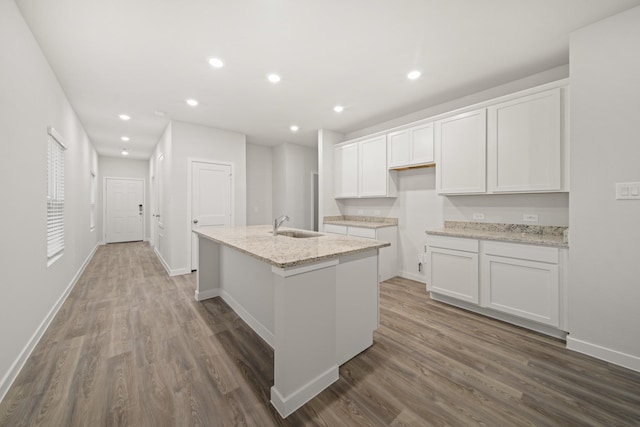 kitchen featuring dark wood-type flooring, sink, light stone countertops, a kitchen island with sink, and white cabinets