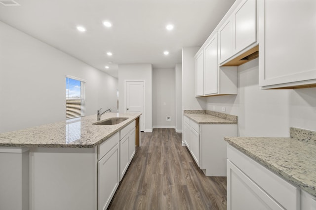 kitchen with an island with sink, light stone countertops, sink, and white cabinets