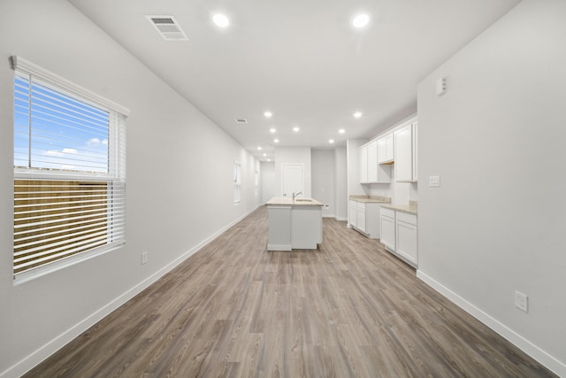 kitchen with white cabinetry, sink, a center island with sink, and light hardwood / wood-style flooring