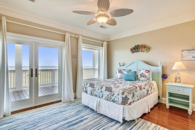 bedroom featuring access to exterior, ceiling fan, wood-type flooring, a water view, and ornamental molding