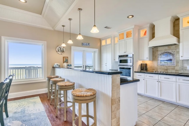 kitchen featuring white cabinets, custom exhaust hood, a kitchen bar, and backsplash