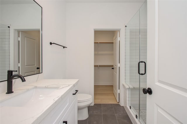 bathroom featuring tile patterned flooring, vanity, toilet, and a shower with door