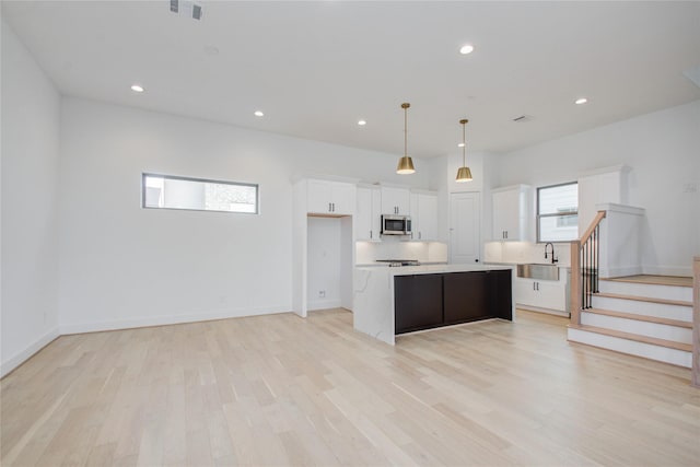 kitchen featuring pendant lighting, white cabinets, light wood-type flooring, tasteful backsplash, and a kitchen island