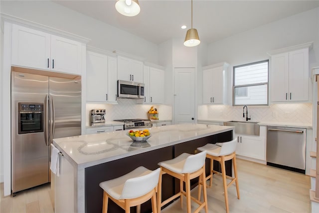 kitchen with stainless steel appliances, sink, decorative light fixtures, a center island, and white cabinetry