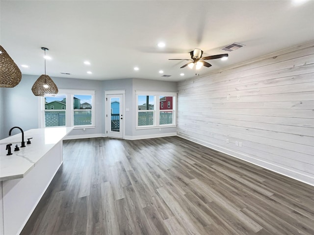 unfurnished living room featuring dark hardwood / wood-style flooring, ceiling fan, and wooden walls