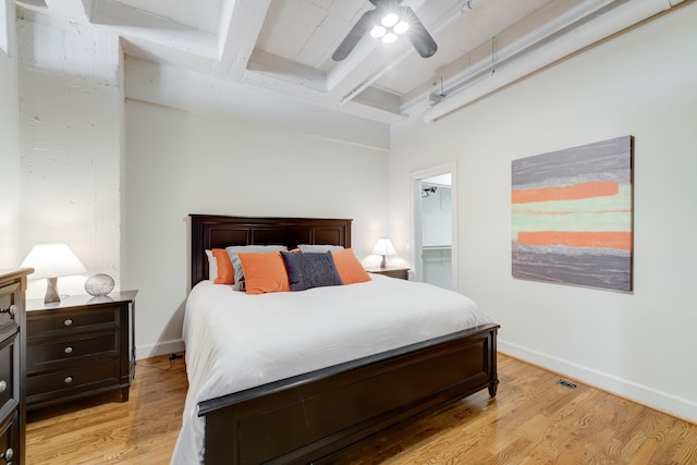 bedroom with beamed ceiling, ceiling fan, light hardwood / wood-style floors, and a walk in closet