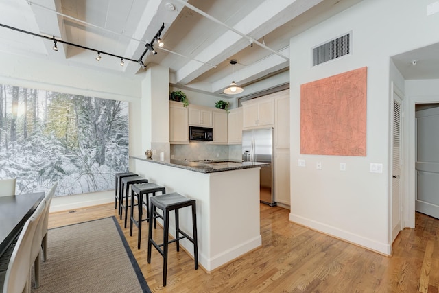 kitchen with dark stone counters, rail lighting, stainless steel fridge, tasteful backsplash, and decorative light fixtures