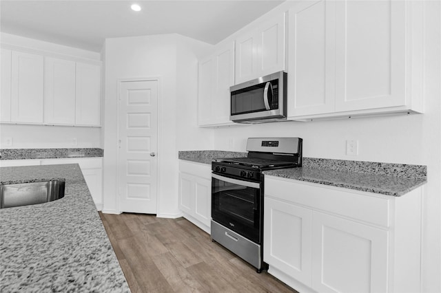 kitchen with white cabinets, stainless steel appliances, light stone counters, and sink