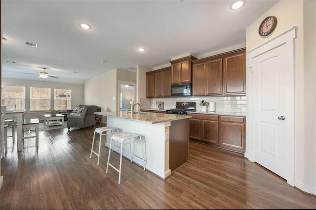 kitchen with a breakfast bar, dark wood-style flooring, a sink, black appliances, and open floor plan