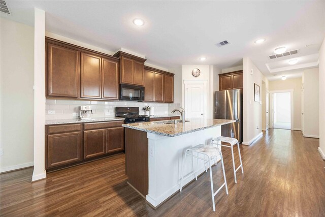 kitchen featuring sink, dark hardwood / wood-style flooring, a kitchen island with sink, light stone counters, and black appliances