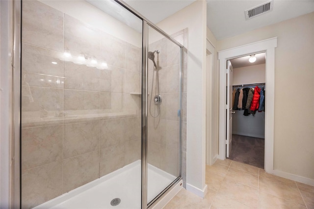 full bathroom featuring tile patterned flooring, visible vents, a walk in closet, baseboards, and a stall shower