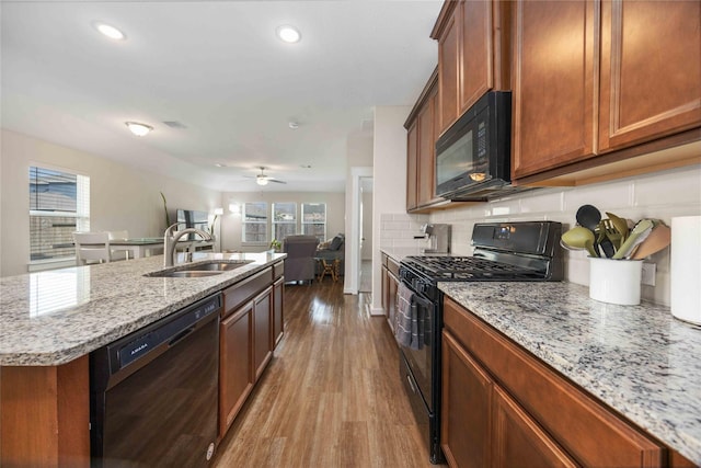 kitchen with backsplash, light stone countertops, wood finished floors, black appliances, and a sink