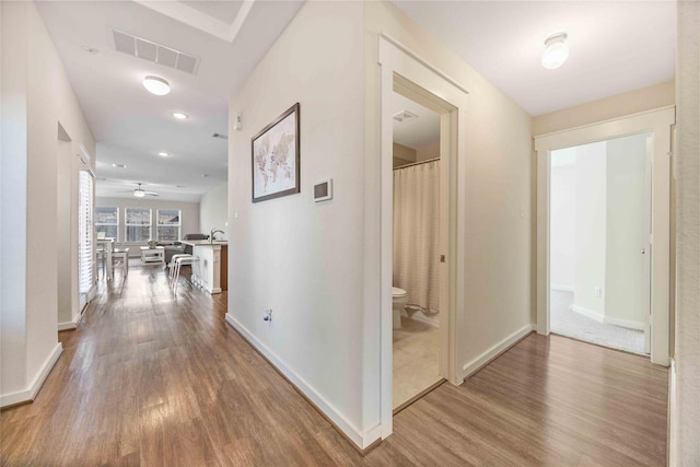 hallway with dark wood-style floors, visible vents, baseboards, and a sink