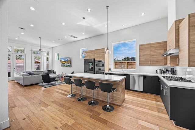 kitchen featuring appliances with stainless steel finishes, a kitchen breakfast bar, decorative light fixtures, light hardwood / wood-style floors, and a kitchen island