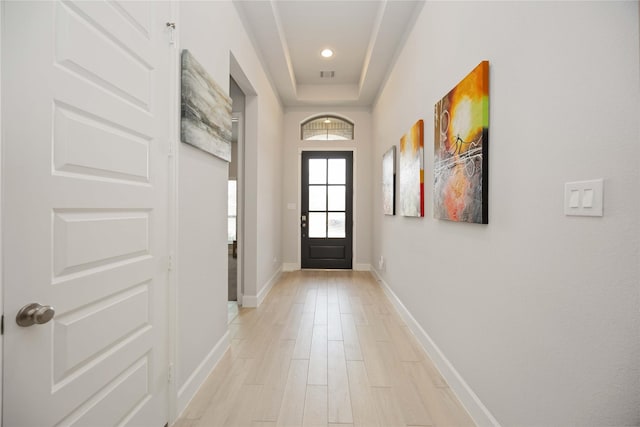 doorway featuring light wood-type flooring and a raised ceiling