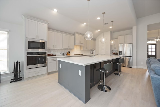 kitchen featuring stainless steel appliances, white cabinets, a center island with sink, and decorative light fixtures