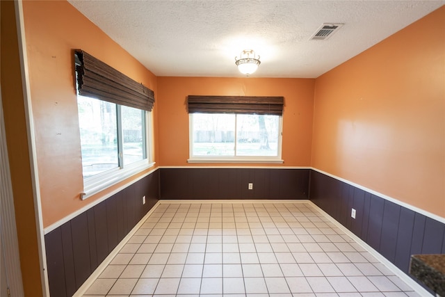 unfurnished room with a wealth of natural light, wood walls, and a textured ceiling