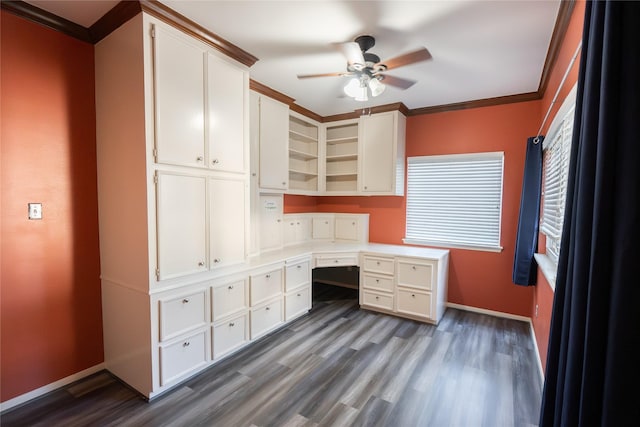 unfurnished office featuring ceiling fan, dark hardwood / wood-style flooring, built in desk, and crown molding