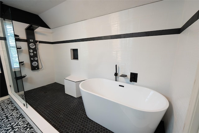 bathroom with vaulted ceiling, a tub to relax in, tile patterned floors, and tile walls