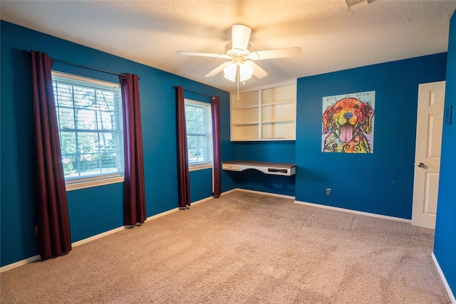 spare room with built in desk, carpet floors, and ceiling fan