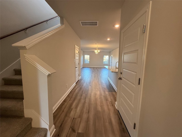 hallway with wood-type flooring and an inviting chandelier