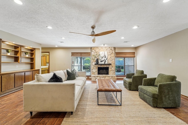 living room featuring a stone fireplace, ceiling fan, a textured ceiling, and light wood-type flooring