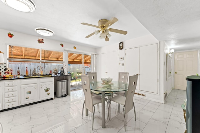 dining space with ceiling fan, sink, and a textured ceiling