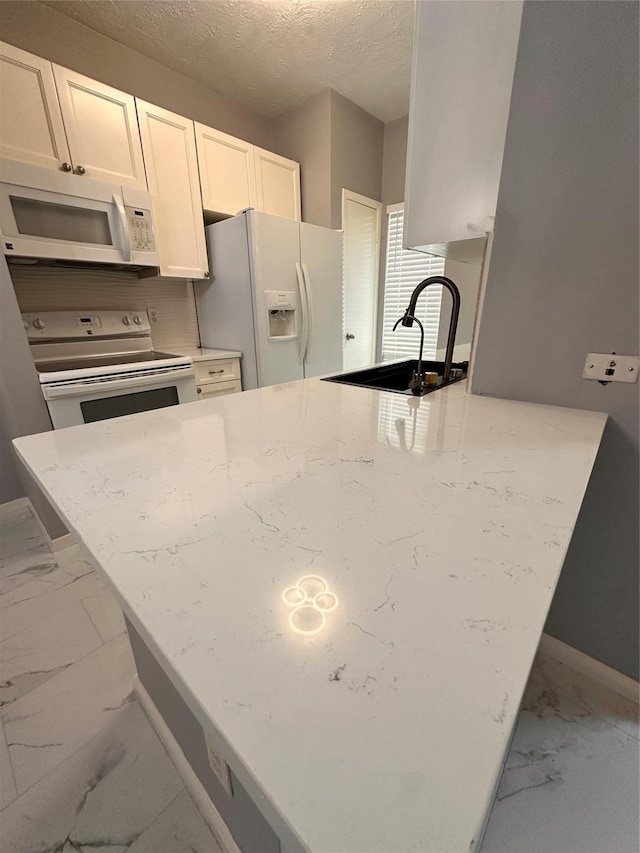 kitchen with white cabinets, white appliances, light stone countertops, and sink