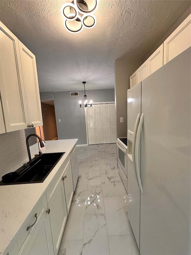 kitchen with white appliances, sink, pendant lighting, an inviting chandelier, and white cabinetry