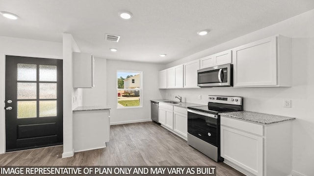 kitchen featuring white cabinets, light wood-type flooring, stainless steel appliances, and light stone counters