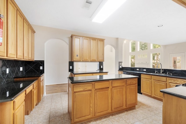 kitchen featuring dishwasher, backsplash, sink, light tile patterned floors, and a kitchen island