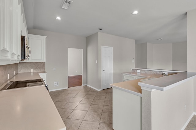 kitchen featuring kitchen peninsula, stove, tasteful backsplash, light tile patterned floors, and white cabinetry