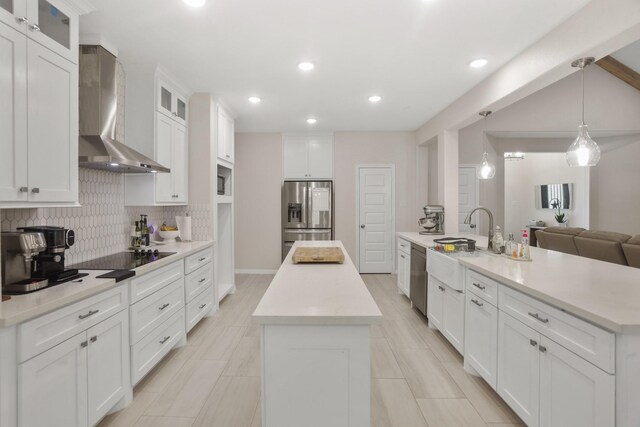 kitchen with wall chimney exhaust hood, stainless steel appliances, a kitchen island with sink, decorative light fixtures, and white cabinetry