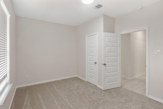 unfurnished bedroom featuring multiple windows, light carpet, and a closet