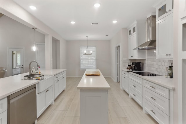 kitchen featuring white cabinets, a kitchen island with sink, wall chimney exhaust hood, and decorative light fixtures