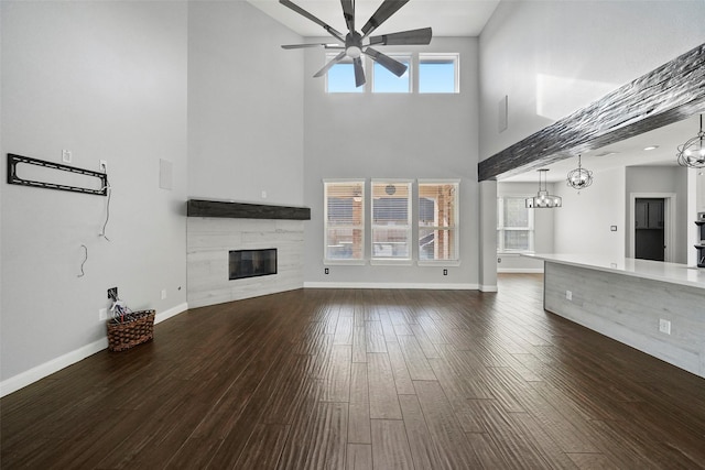 unfurnished living room featuring a tile fireplace, dark hardwood / wood-style flooring, ceiling fan with notable chandelier, and a healthy amount of sunlight