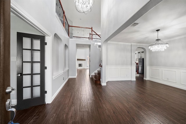 foyer entrance featuring dark wood-type flooring, crown molding, a high ceiling, and an inviting chandelier