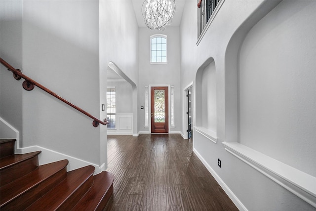 entrance foyer with dark hardwood / wood-style flooring, a towering ceiling, and a chandelier