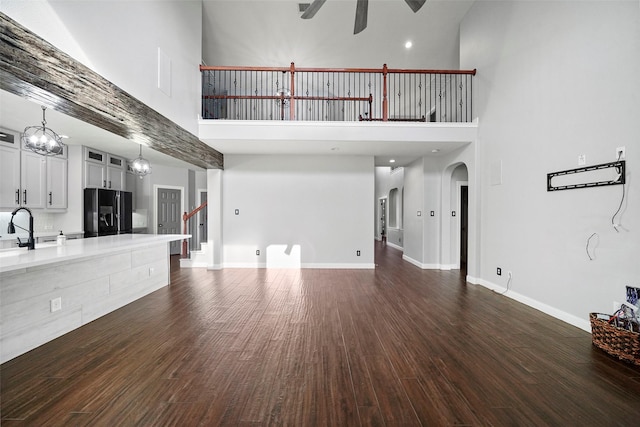 unfurnished living room with ceiling fan, sink, dark wood-type flooring, and a high ceiling