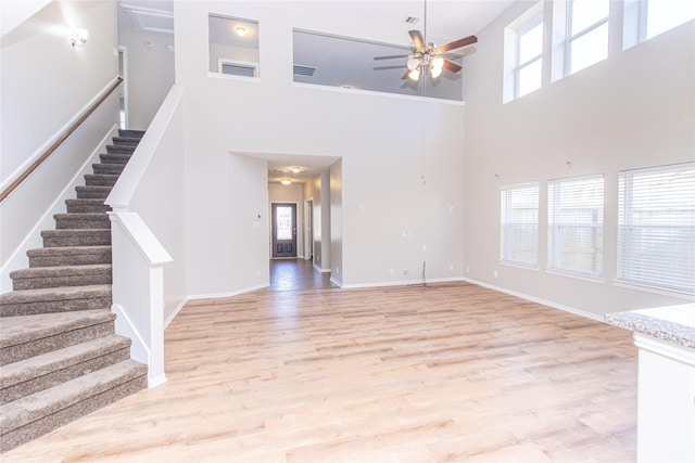 unfurnished living room featuring a towering ceiling, light hardwood / wood-style floors, and ceiling fan