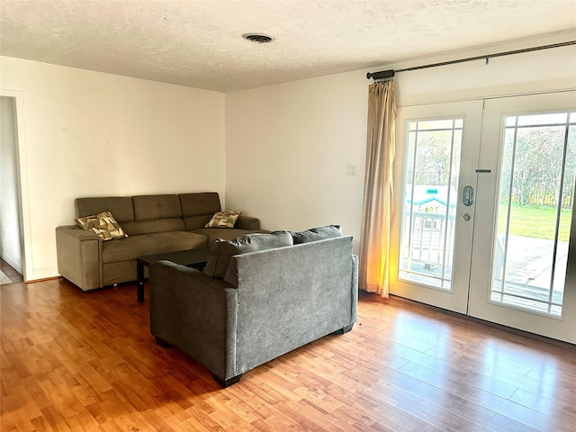 living area with light wood finished floors, visible vents, a textured ceiling, and french doors