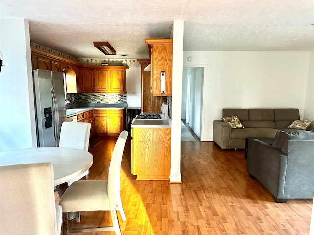 kitchen with light wood-style floors, stainless steel refrigerator with ice dispenser, decorative backsplash, and open floor plan