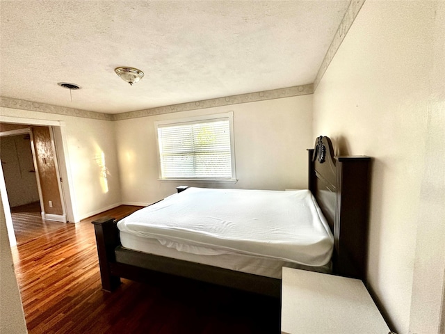 bedroom featuring a textured ceiling, baseboards, and wood finished floors