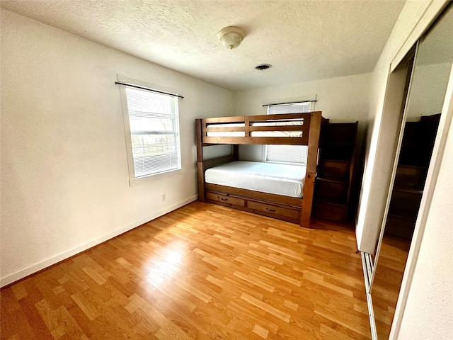 unfurnished bedroom with light wood-type flooring, a closet, baseboards, and a textured ceiling