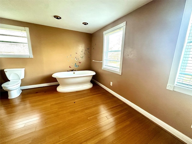 bathroom featuring toilet, a freestanding bath, baseboards, and wood finished floors