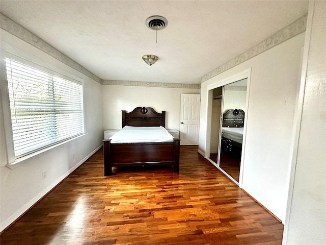 bedroom with a closet, wood finished floors, visible vents, and baseboards