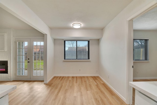 interior space featuring a textured ceiling, light wood-type flooring, a fireplace, and french doors