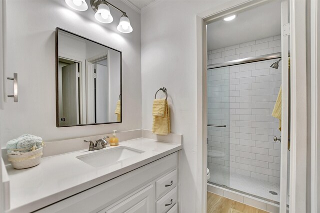 bathroom with ornamental molding, vanity, a shower with door, hardwood / wood-style floors, and toilet