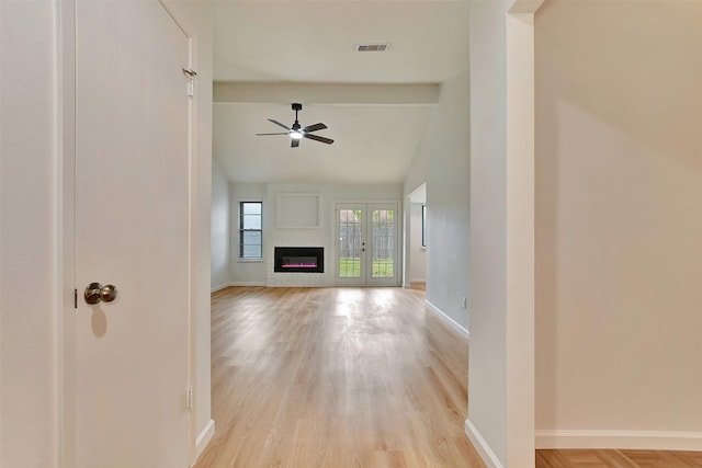 unfurnished living room featuring french doors, light wood-type flooring, a large fireplace, ceiling fan, and lofted ceiling with beams